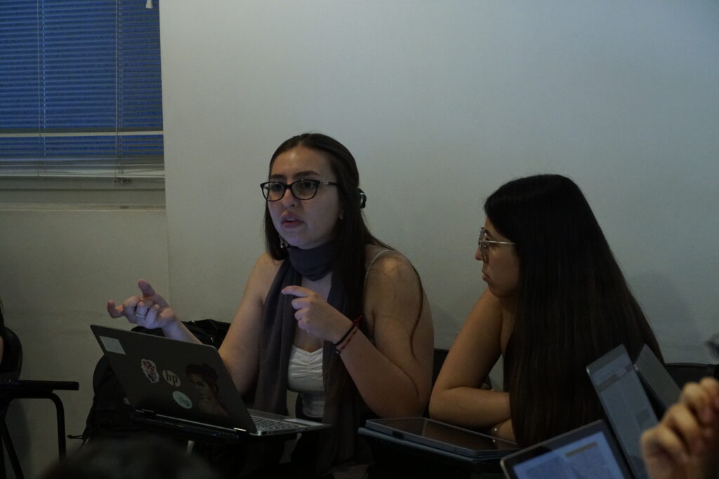 Dos estudiantes de la clínica jurídica sentadas en sus pupitres durante una clase.